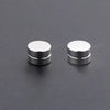 A pair of silver crystal magnetic stud earrings for men resting on a dark gray surface.