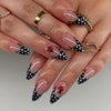 A close-up of a hand displaying almond-shaped press-on false nails with a white and black polka dot design featuring small re