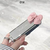 A hand holds a silver folding mini hair comb with a mirror and a pink bow for styling.