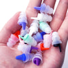 Una mano sostiene numerosos tapones para los oídos de silicona en varios colores, incluyendo morado, azul, blanco y rosa.