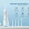 A white portable water dental flosser device is displayed on a counter with various dental tools and accessories.