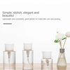 Three clear glass refillable push-down pump dispenser bottles with white pump tops displayed on a wooden surface.
