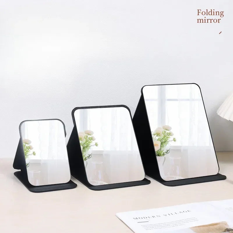 A set of black folding mirrors with clear reflective surfaces displayed on a light surface.