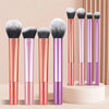 An arrangement of eight makeup brushes in various shades of pink and purple standing upright on a white surface.