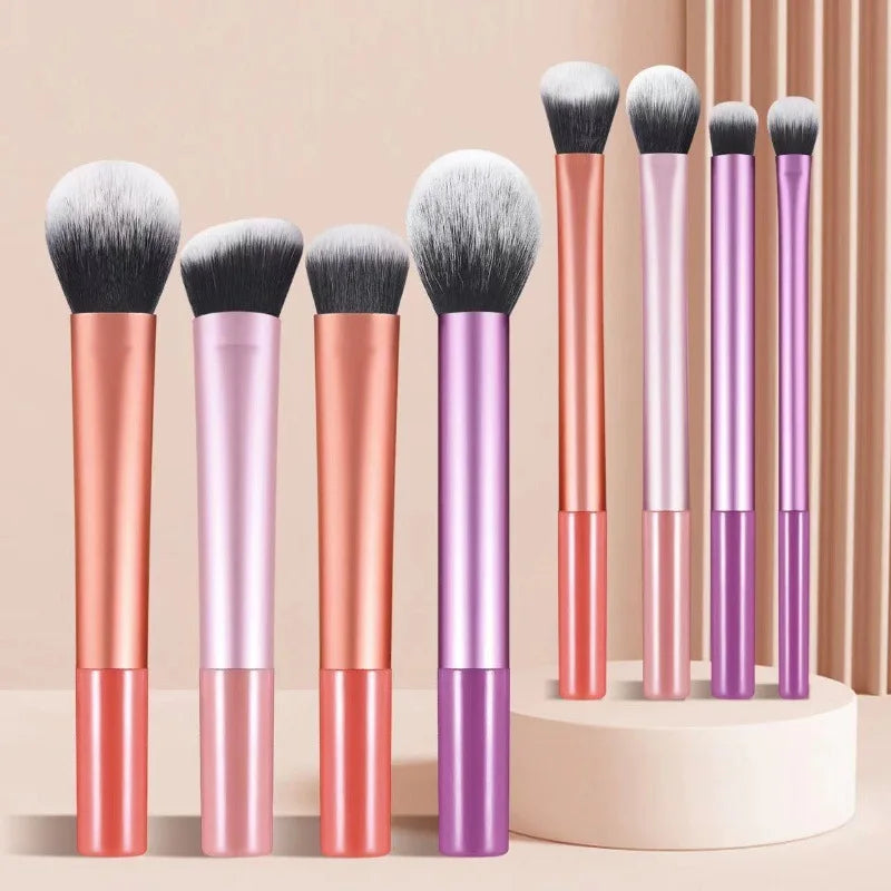 An arrangement of eight makeup brushes in various shades of pink and purple standing upright on a white surface.