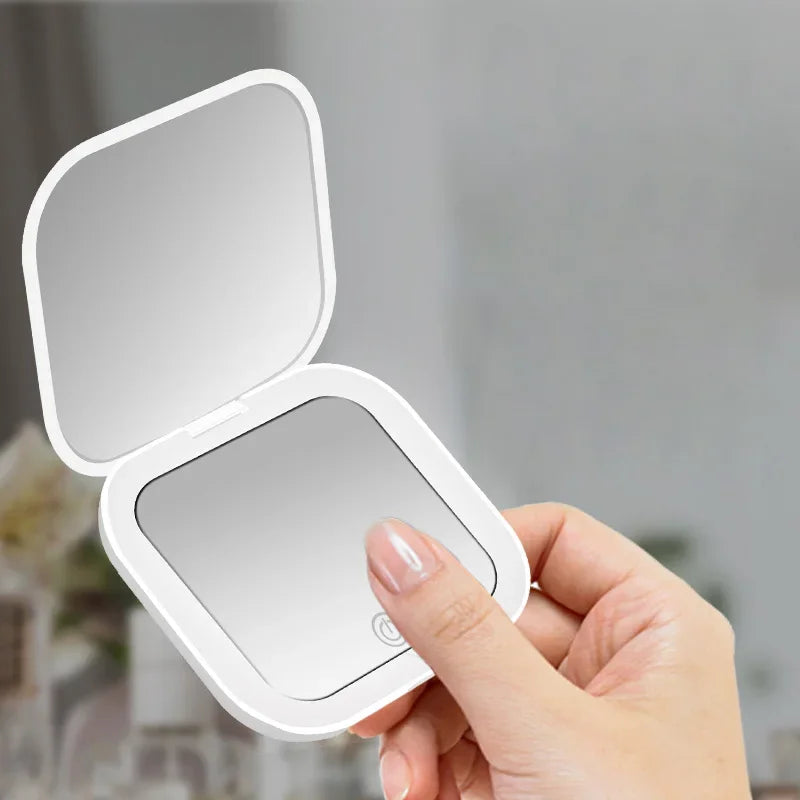 Une main tient un miroir de vanité pliable ouvert avec une lumière LED intégrée.