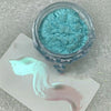 A jar of turquoise glitter powder next to a swatch showing a gradient of mint green and pink hues.