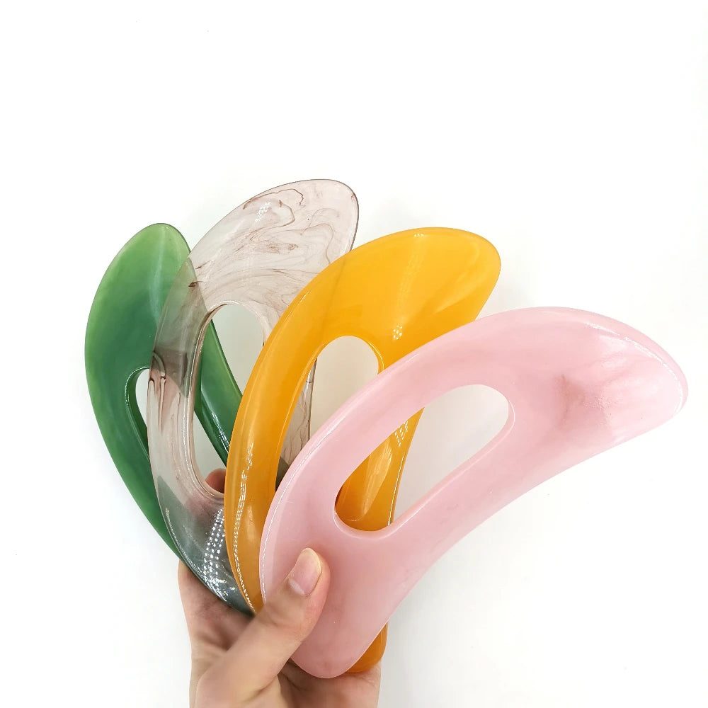 Une main tient quatre pierres naturelles de massage Guasha dans des tons de vert, beige, orange et rose.