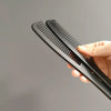 A hand holds a black anti-static carbon hair combs set with multiple teeth against a gray background.