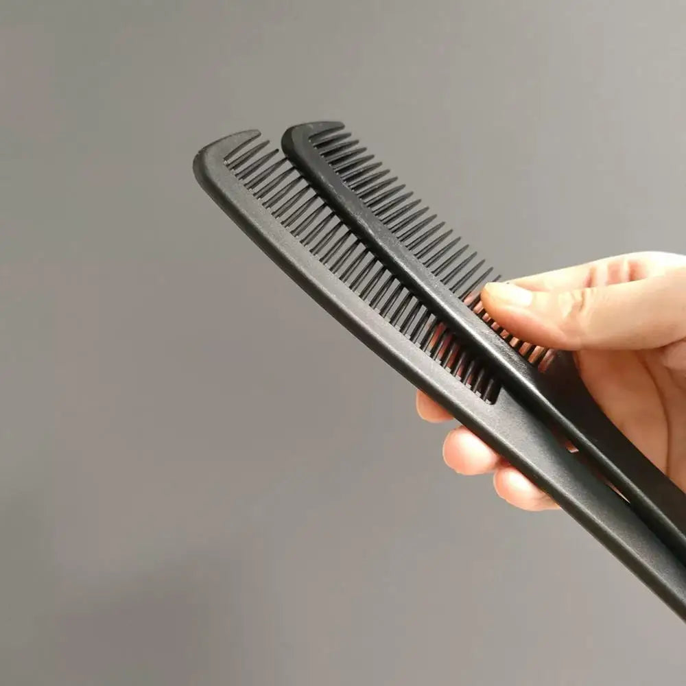 A hand holds a black anti-static carbon hair combs set with multiple teeth against a gray background.