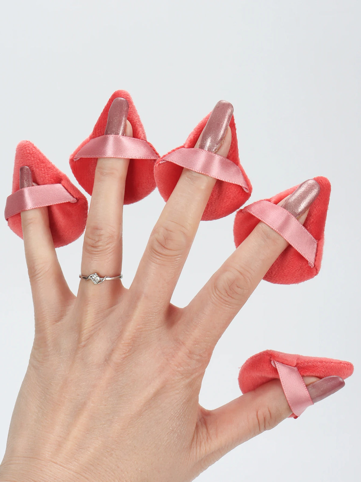 Une main présente un ensemble de puffs triangulaires en tissu rose corail avec des rubans satinés.