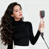 A woman is using a pink hair curling tool to style her long, dark hair.
