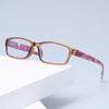 Un par de gafas de lectura de capodomo con detalles en rosa y morado sobre una superficie blanca.