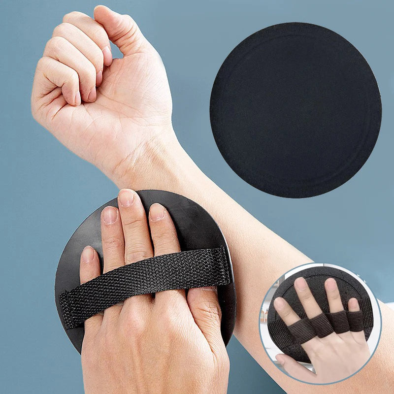 A hand is shown holding a black silicone shower brush and a circular black cleaning pad against a gray background.