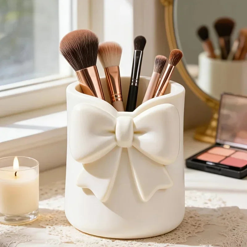 Organisateur en céramique blanche contenant divers pinceaux et outils de maquillage sur une surface claire.