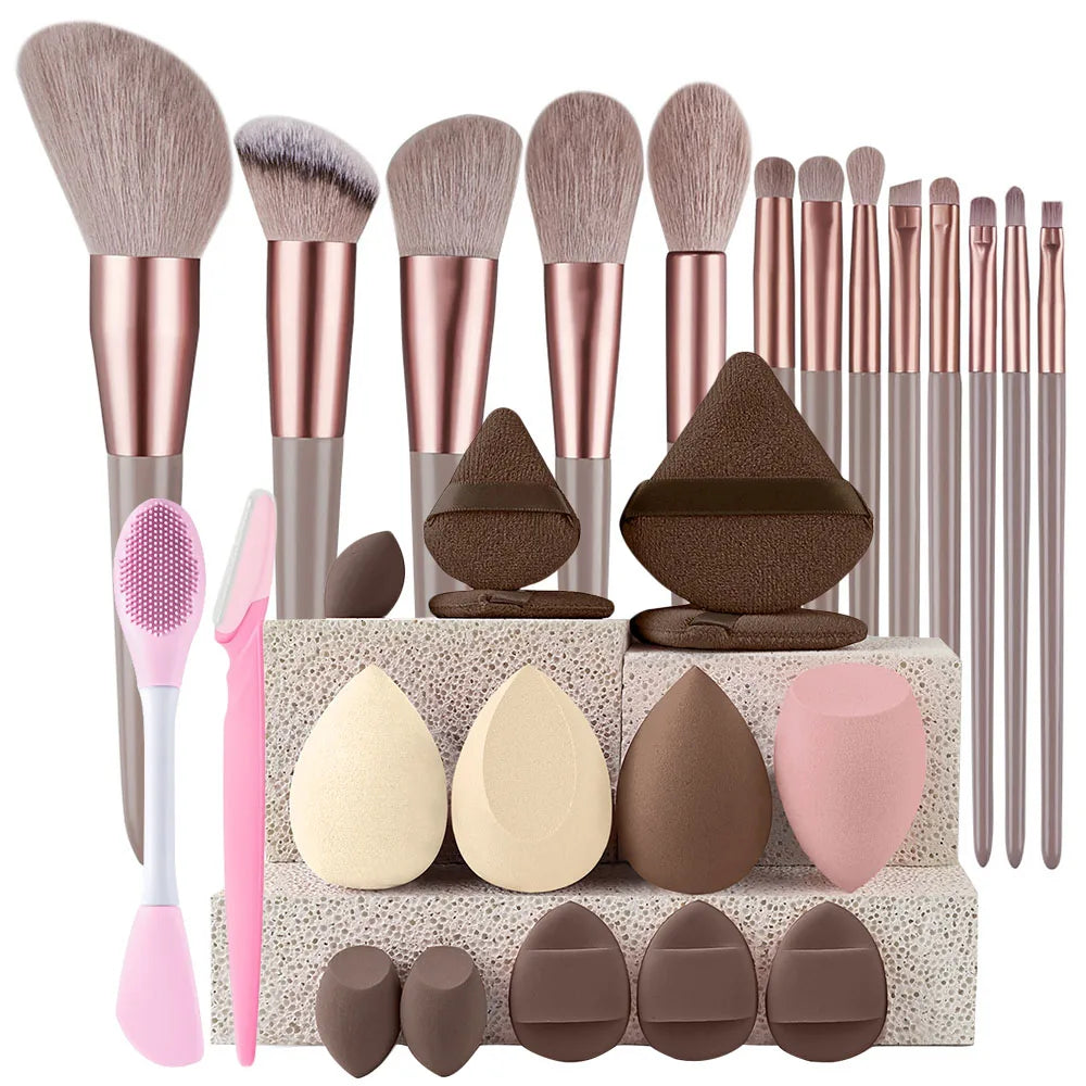 A collection of makeup brushes and sponges in various shades of pink, brown, and nude tones displayed on a box.