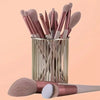 A collection of 13 professional makeup brushes in rose gold and natural tones stored in a cylindrical metal holder.