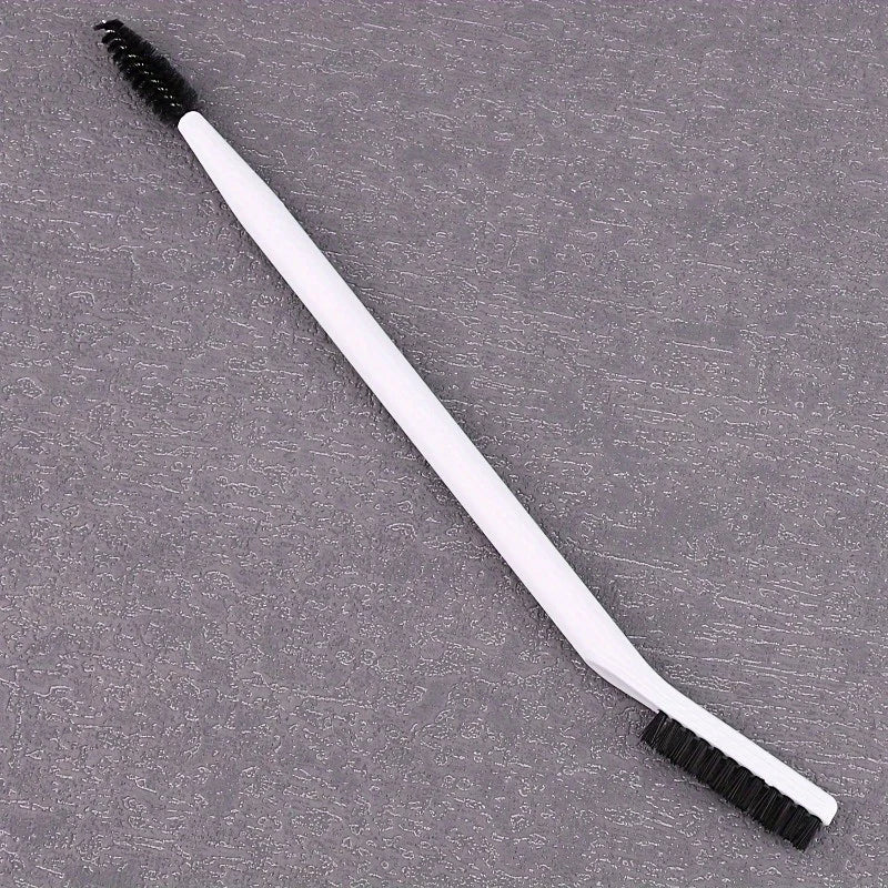 A white dual-ended eyelash curler and brow brush set lying on a gray surface.