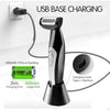 A black electric body grooming shaver with a silver charging base and a green battery is shown next to a wall outlet.