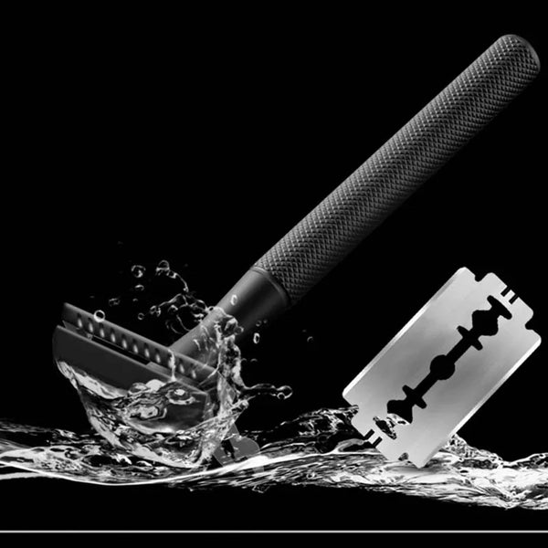 Primer plano de una navaja de seguridad metálica negra con cuchilla visible y agua salpicando abajo.