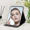 A portable folding makeup mirror showing a woman's face, held in a light green glass vase.