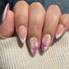 A close-up of a hand displaying press-on acrylic nails decorated with delicate purple and white floral designs.