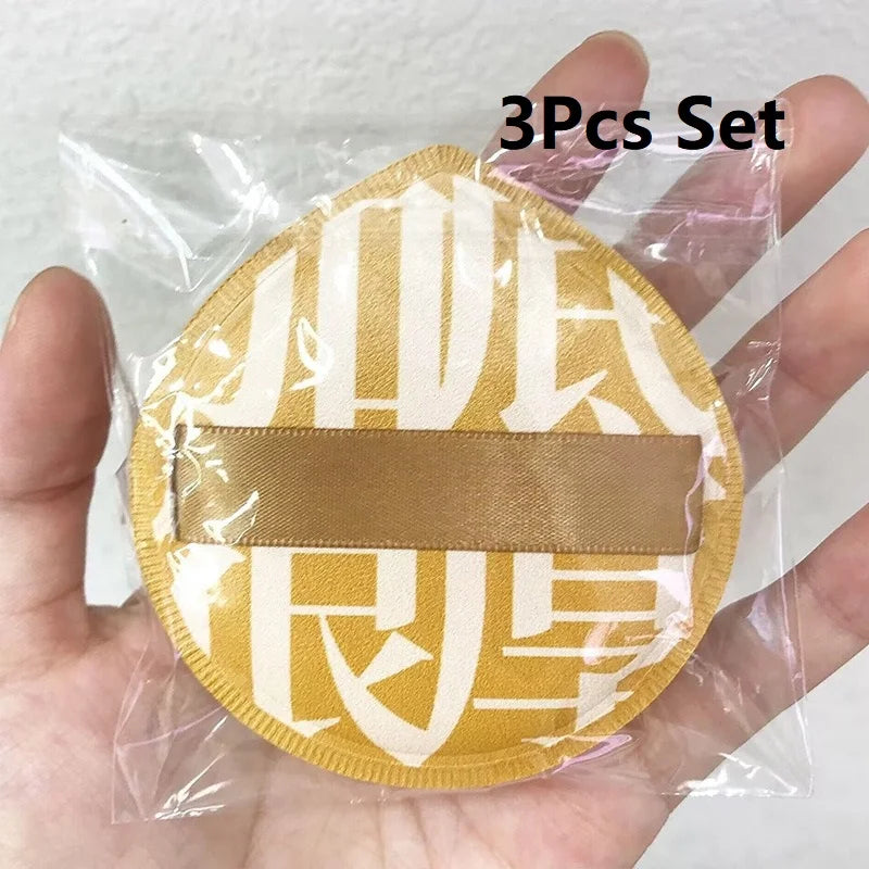 A set of three beige makeup puffs packaged in a clear plastic bag being held by a hand.