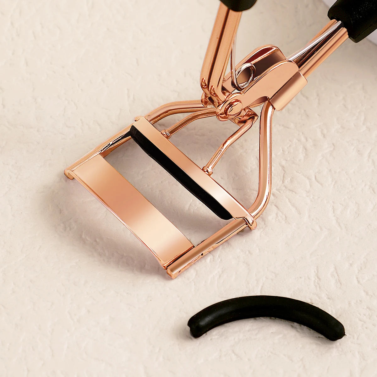 A close-up of a professional stainless steel eyelash curler set with gold-toned metal and black rubber grips.