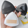 A hand holds a black triangular cosmetic foundation puff brush and a white puff brush.