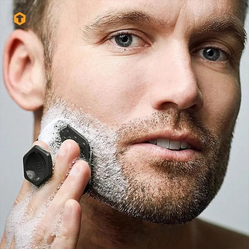 A man is using a silicone facial cleaning brush to apply foam on his face.