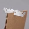 A close-up of stainless steel single-sided shaving razor blades resting on a brown leather or cardboard product.