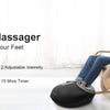 A woman is using a black shiatsu foot massager on her feet while relaxing in a wooden chair.