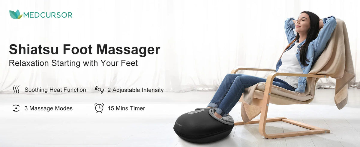 A woman is using a black shiatsu foot massager on her feet while relaxing in a wooden chair.