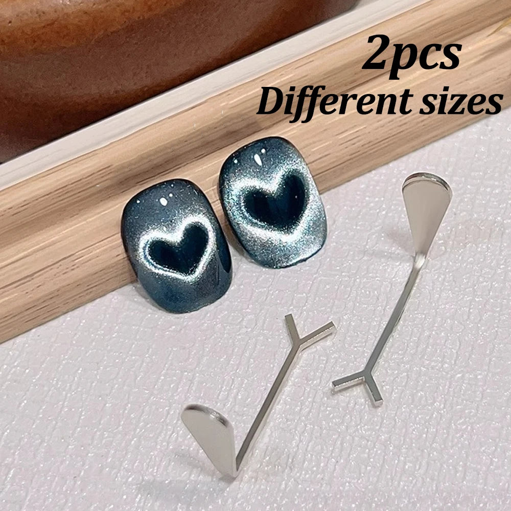 Deux aimants en forme de cœur à ongles de différentes tailles sont exposés sur une surface en bois.
