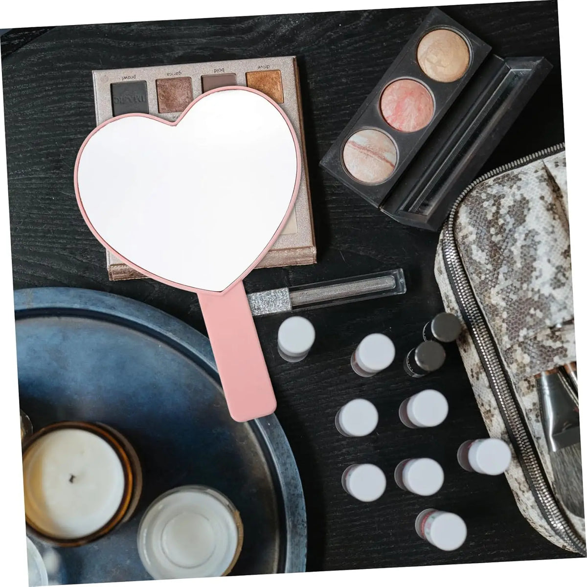 Miroir à cils en forme de cœur à main avec poignée rose, présenté sur une surface sombre avec maquillage et une fermeture écl