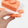 A hand holds an orange multi-sided nail and cuticle buffing file with white stripes on a white background.