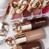 A collection of Rare Beauty liquid bronzer contour foundation sticks in various shades and packaging.