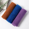 Three rolled reusable exfoliating bath sponges in shades of brown, blue, and purple