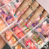 A hand displays a set of press-on nails featuring pink, green, and purple candy colors in clear packaging.