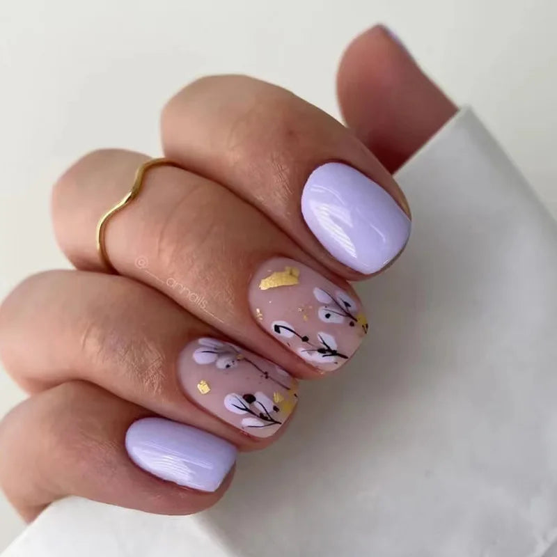 A hand displays a set of blue floral press-on false nails with white and gold accents on a white background.
