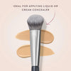 A silver precision concealer brush shown with swatches of beige liquid or cream concealer on a light background.