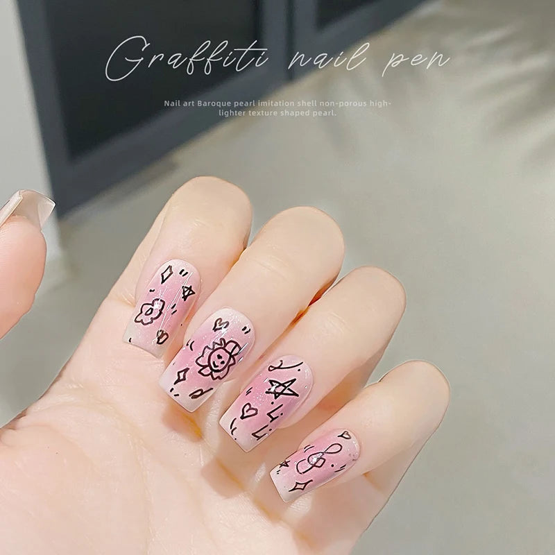 A hand displays detailed nail art featuring pink and white graffiti designs on the fingernails.