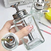 A hand holds a clear glass pressure bottle dispenser for nail art, showing the pump mechanism and liquid inside.