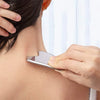 A hand is using a stainless steel gua sha tool on the neck and collarbone area of a person's skin.