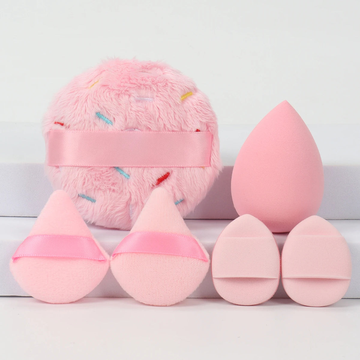 Un ensemble de poudre de couleur rose, comprenant une mèche rose duveteuse et plusieurs pois roses en forme d'œuf.
