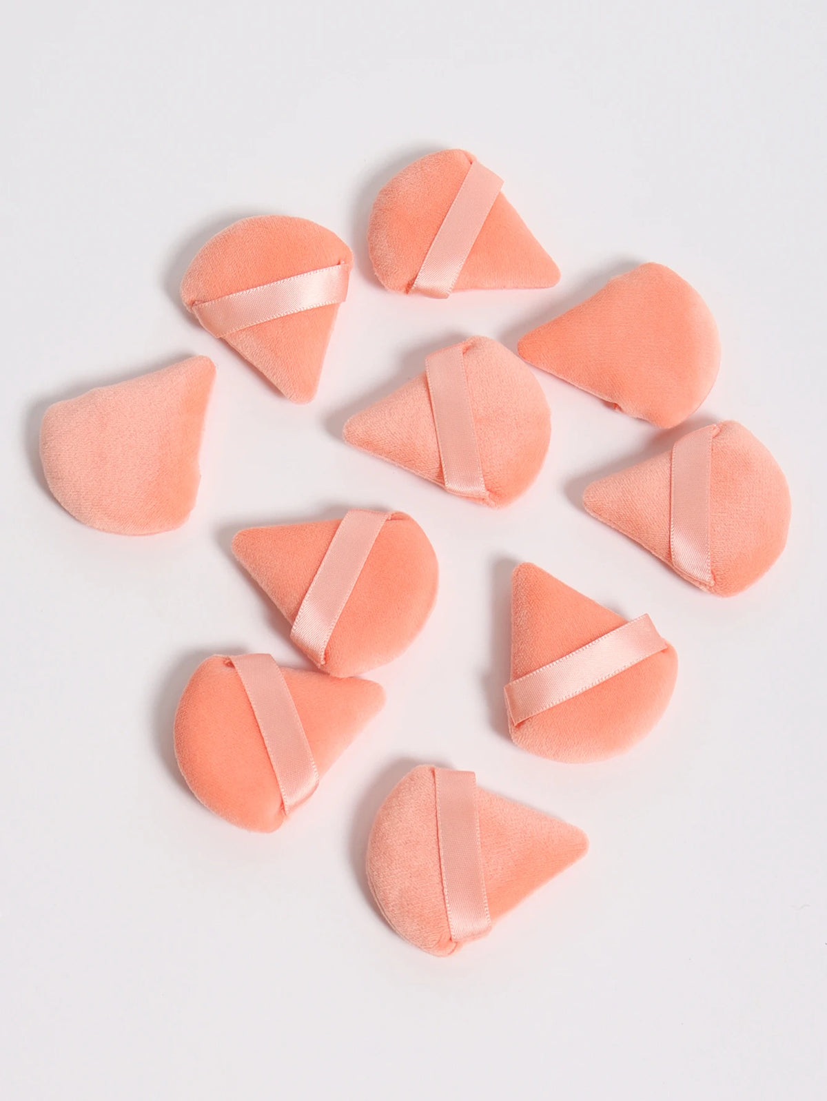 Un set de trois puffs triangulaires roses avec des rubans de satin sur fond blanc.