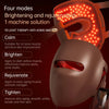 A close-up of an orange LED facial mask device with multiple light points illuminating a brown face mask.