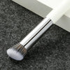A professional makeup brush with a silver ferrule and white bristles resting on a dark gray textured surface.