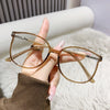 Une main tient une paire de lunettes à monture dorée en forme de chat, sur un fond blanc et duveteux.