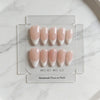 A set of pink handmade press-on nails in a French almond style displayed on a clear plastic tray.